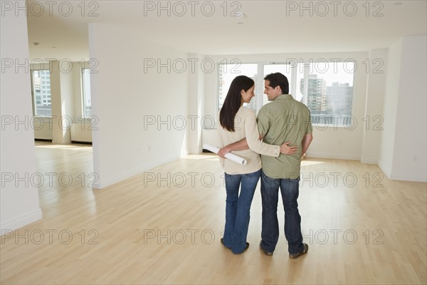 Rear view of couple with blueprints in empty house.