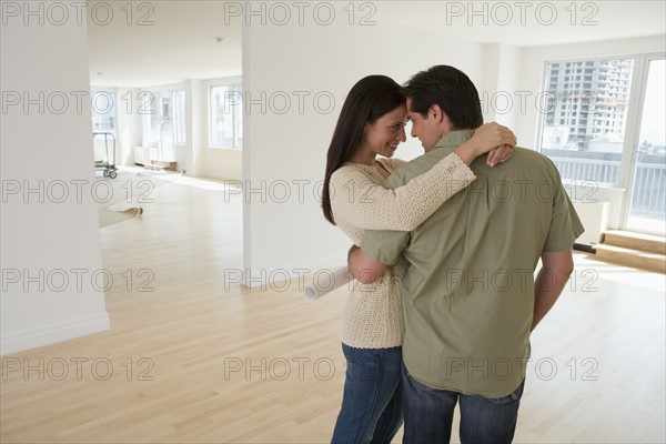 Couple hugging and holding blueprints in empty house.