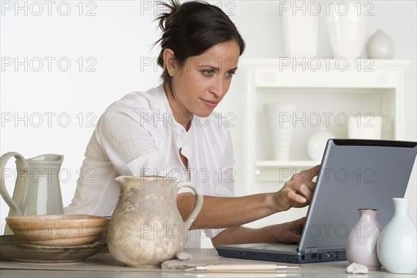 Woman using laptop next to pottery.