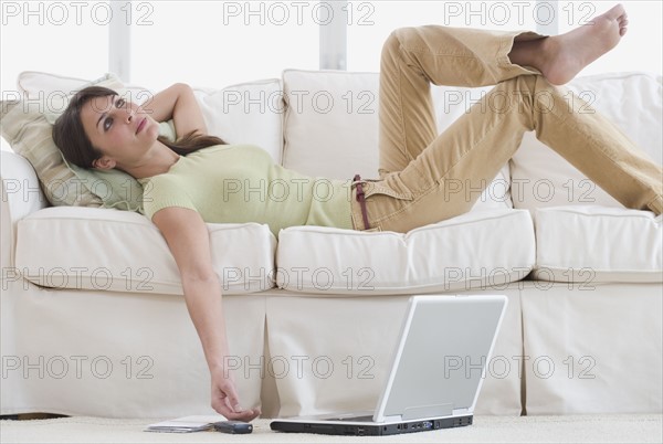 Woman laying on sofa with laptop on floor.