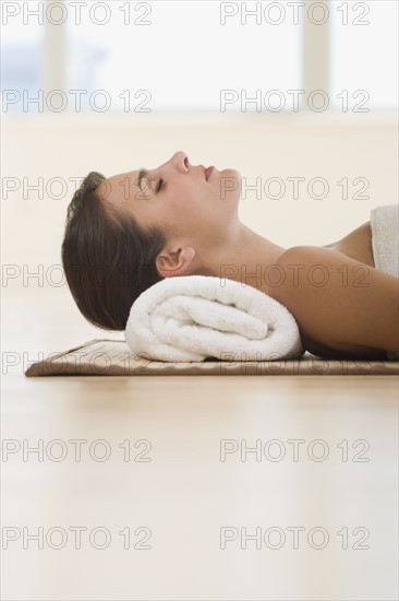Woman laying on mat with rolled towel under neck.