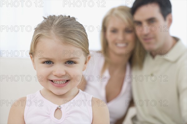 Girl smiling with parents in background.