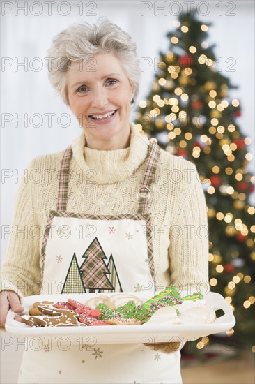 Senior woman holding tray of Christmas cookies.