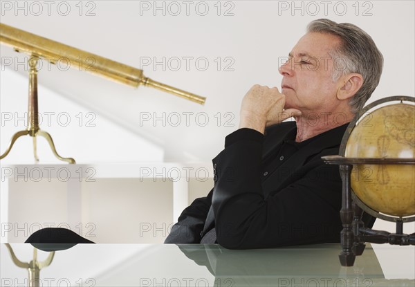 Senior businessman next to globe and telescope.