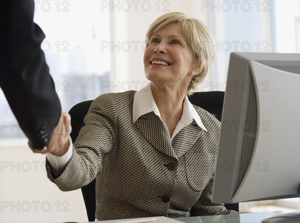 Senior businesswoman shaking hands at desk.