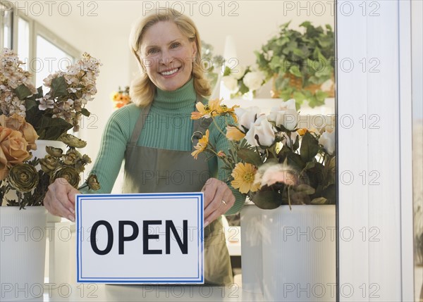 Female florist hanging Open sign in window.