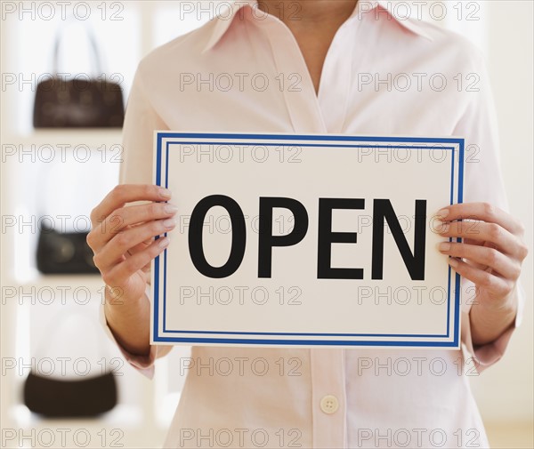 Woman holding Open sign in boutique.