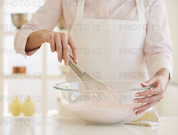 Woman wearing apron and mixing batter .