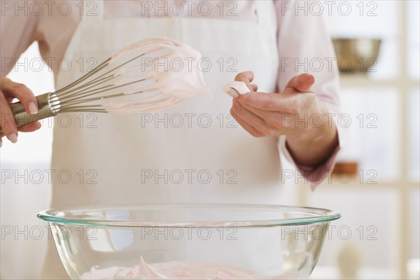 Woman wiping batter from whisk with finger.