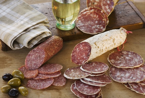 Sliced sausages and olives on table.