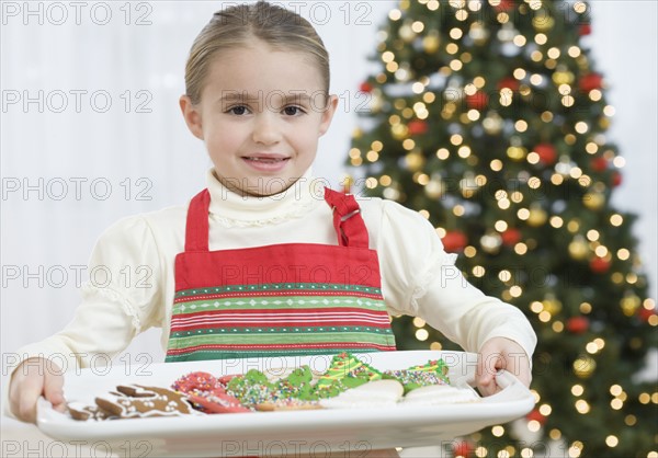 Girl carrying tray of Christmas cookies.