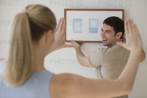 Couple hanging picture on wall.