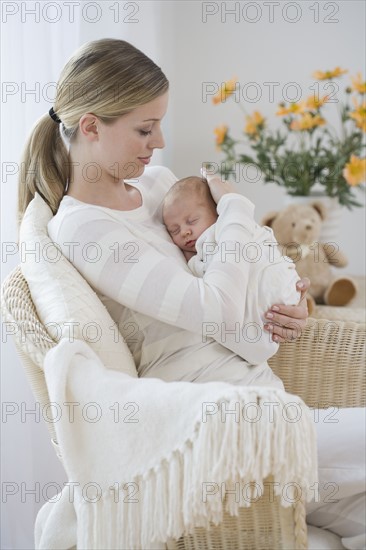 Mother rocking newborn baby in chair.