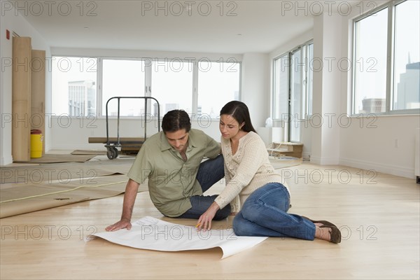 Couple looking at blueprints on floor in new house.