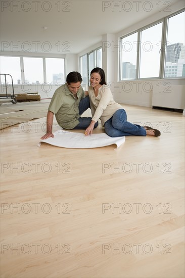 Couple looking at blueprints on floor in new house.