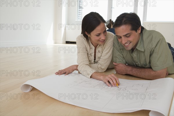 Couple laying on floor looking at blueprints.