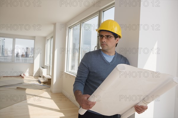 Man wearing hard hat and holding blueprints in house.