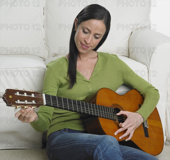 Woman playing guitar on sofa.