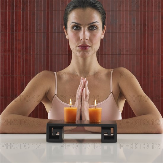 Woman praying behind tray with lit candles.