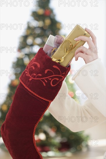 Woman stuffing gifts into Christmas stocking.