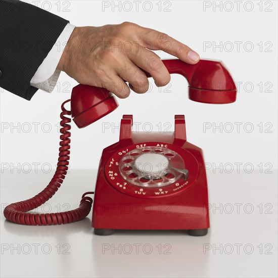 Close up studio shot of man picking up rotary telephone.