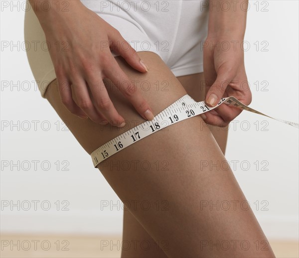 Woman in underwear measuring thigh.