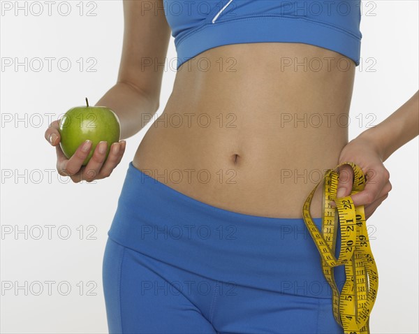 Woman in athletic gear holding apple and tape measure.