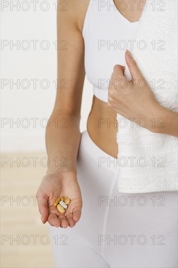 Woman in athletic gear holding vitamins in hand.