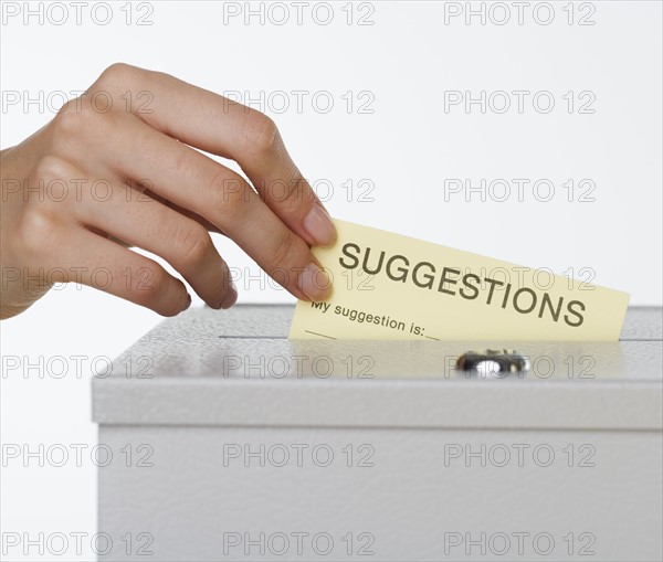 Close up of woman's hand putting card in suggestion box.