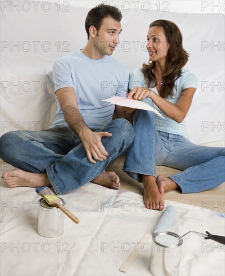 Couple sitting on tarp looking at paint swatches.