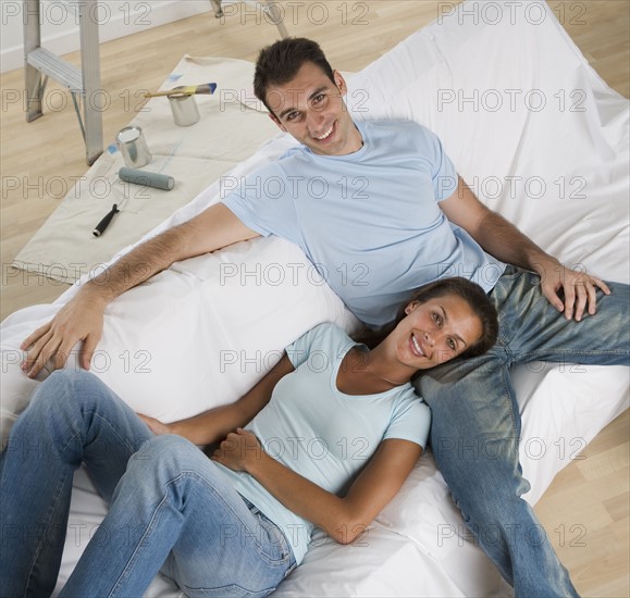 Couple on sofa with paint cans and paintbrushes on floor.