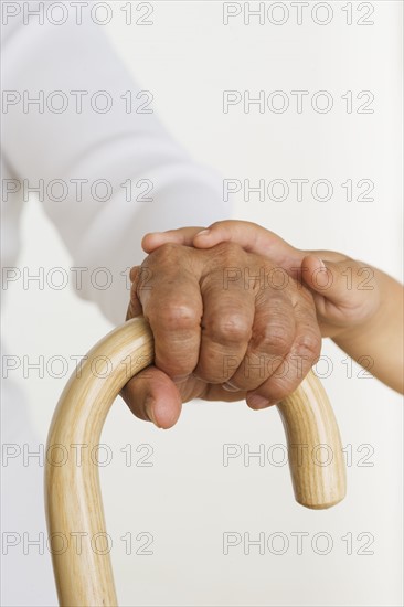 Child's hand laying hand of senior holding cane.