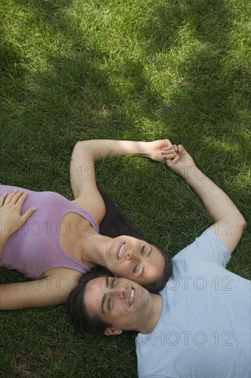 Couple laying with heads together on grass.