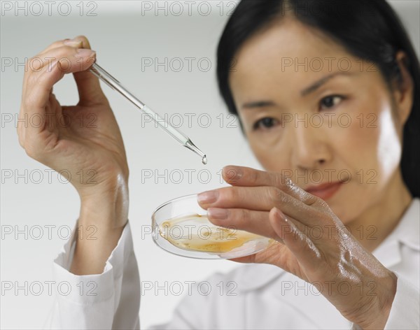 Asian woman dropping liquid into petri dish.