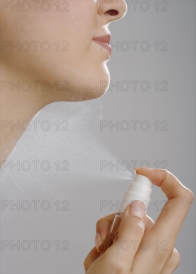 Close up of woman spraying perfume on neck.