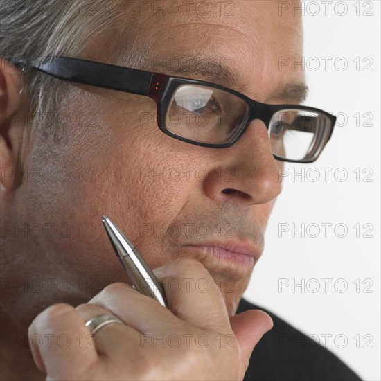 Close up of man holding pen with chin in hand.