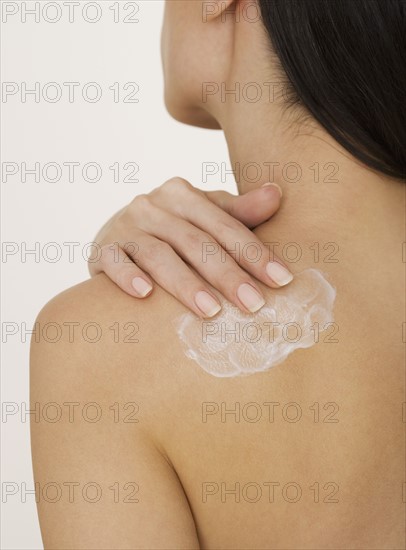 Woman applying lotion to back.