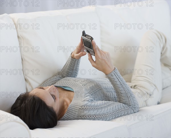 Woman laying on sofa using electronic organizer.
