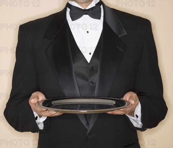 Waiter in tuxedo holding silver platter.