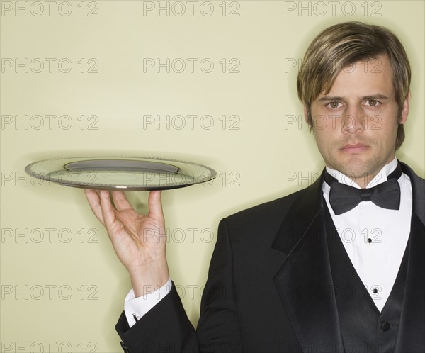 Waiter in tuxedo holding silver platter.