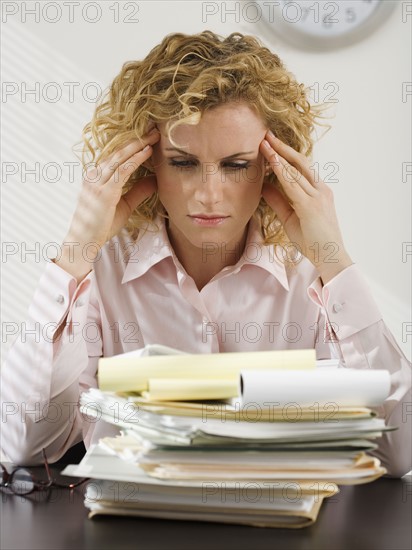 Businesswoman rubbing temples and looking at paperwork.