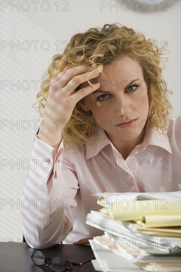 Businesswoman rubbing temple and looking at paperwork.