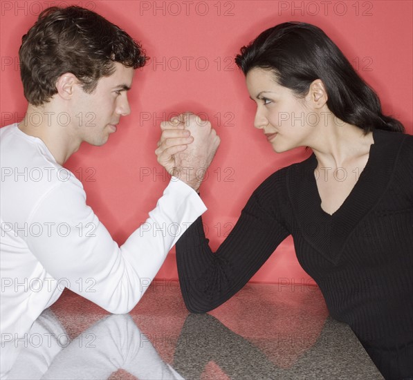 Couple arm wrestling on table.