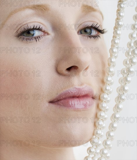 Woman with pearl necklace against face.