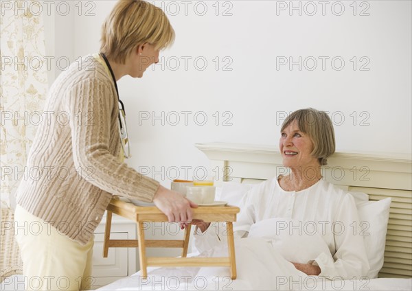 Nurse bringing senior woman breakfast in bed.