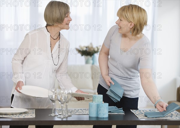 Mother and adult daughter setting table.