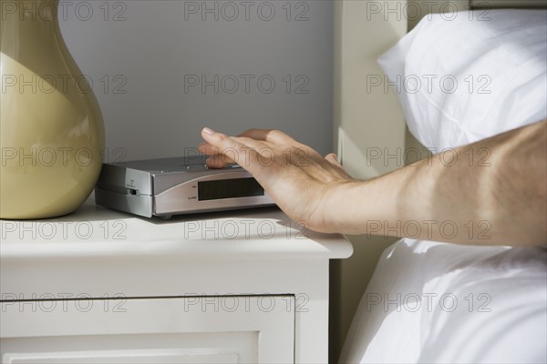 Man touching alarm clock from bed.