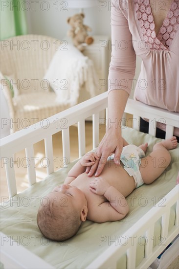 Mother touching baby in crib.