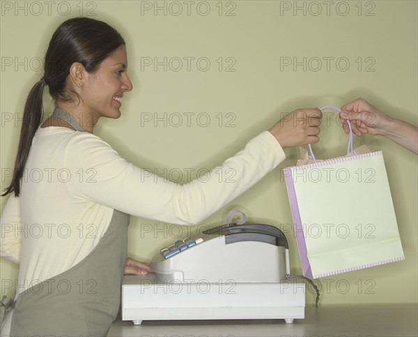 Indian female clerk handing shopping bag.