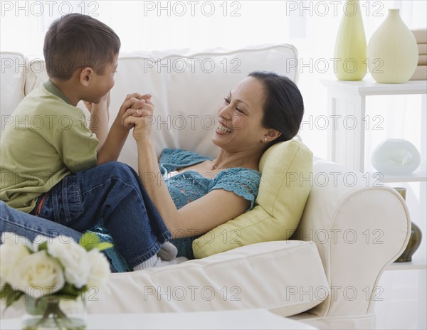 Asian mother and son playing on sofa.